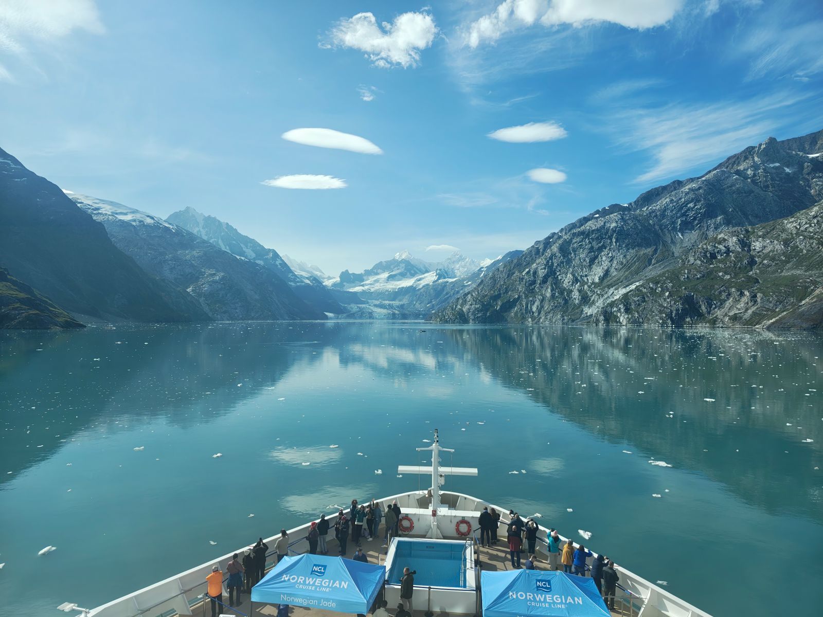 Passengers on a ship&rsquo;s bow sailing into Glacier Bay, Alaska, between snowy mountains