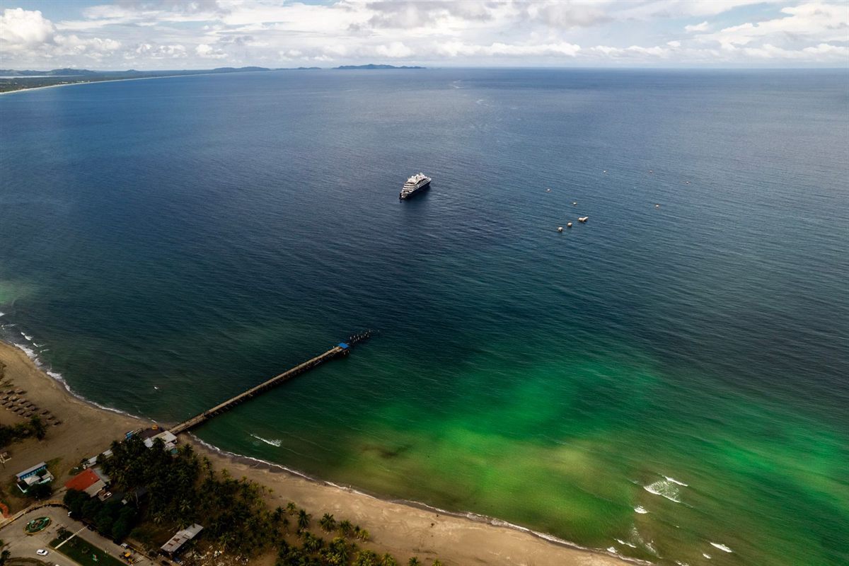 Aerial view of a long tropical beach and pier in Honduras with a small ship anchored offshore