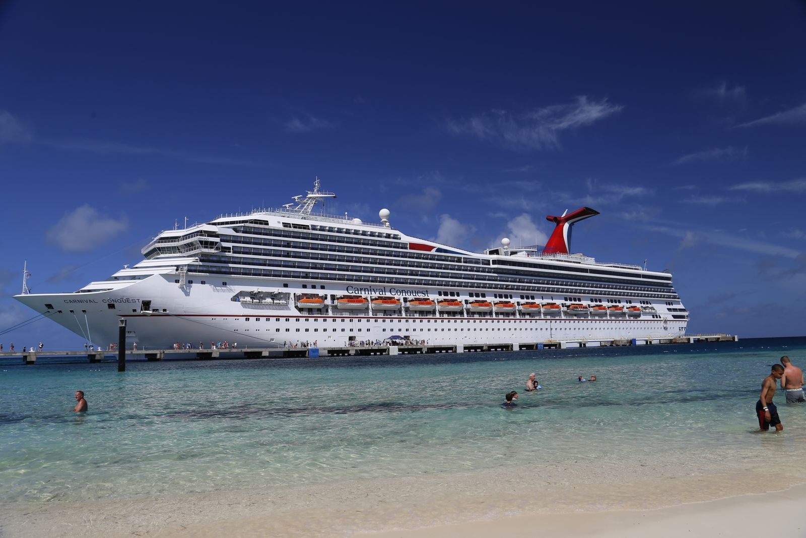 A Carnival cruise ship docked beside a turquoise beach with swimmers, the trip a Carnival cruise survey asks about