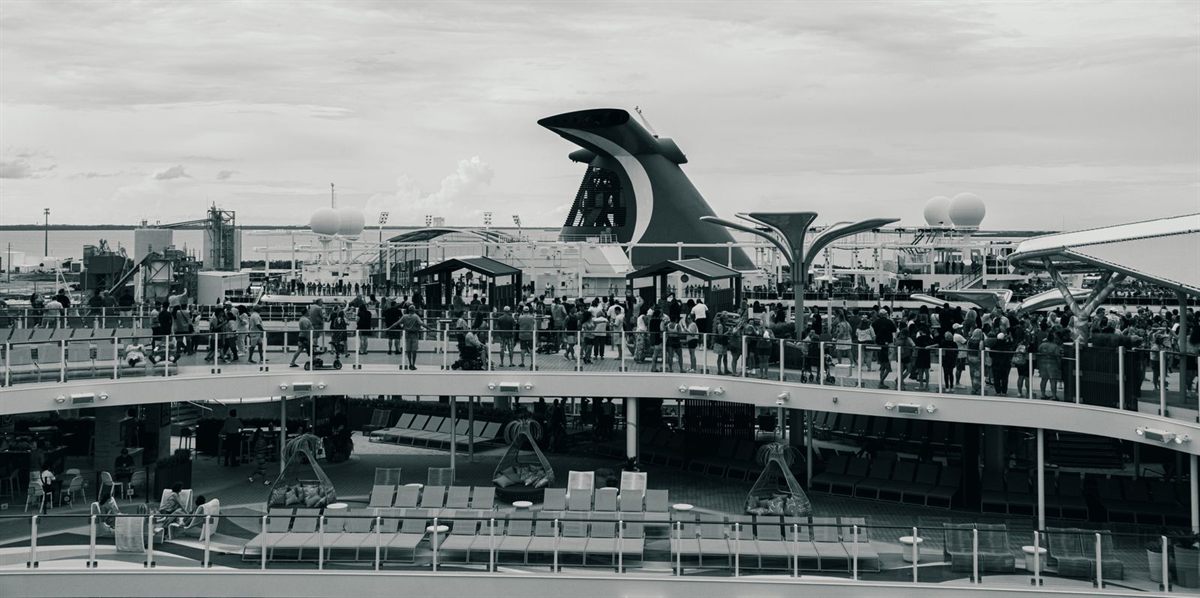 Black and white view of a busy Carnival pool deck below the ship’s winged funnel
