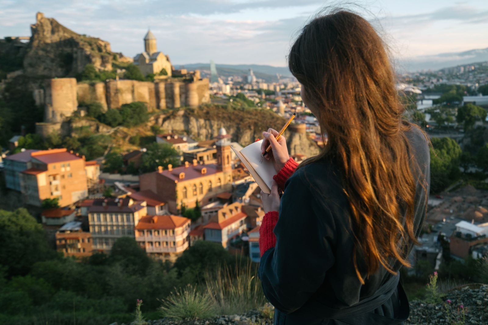 A traveller writing notes while looking over an old hillside town, weighing Consumer Reports best cruise lines