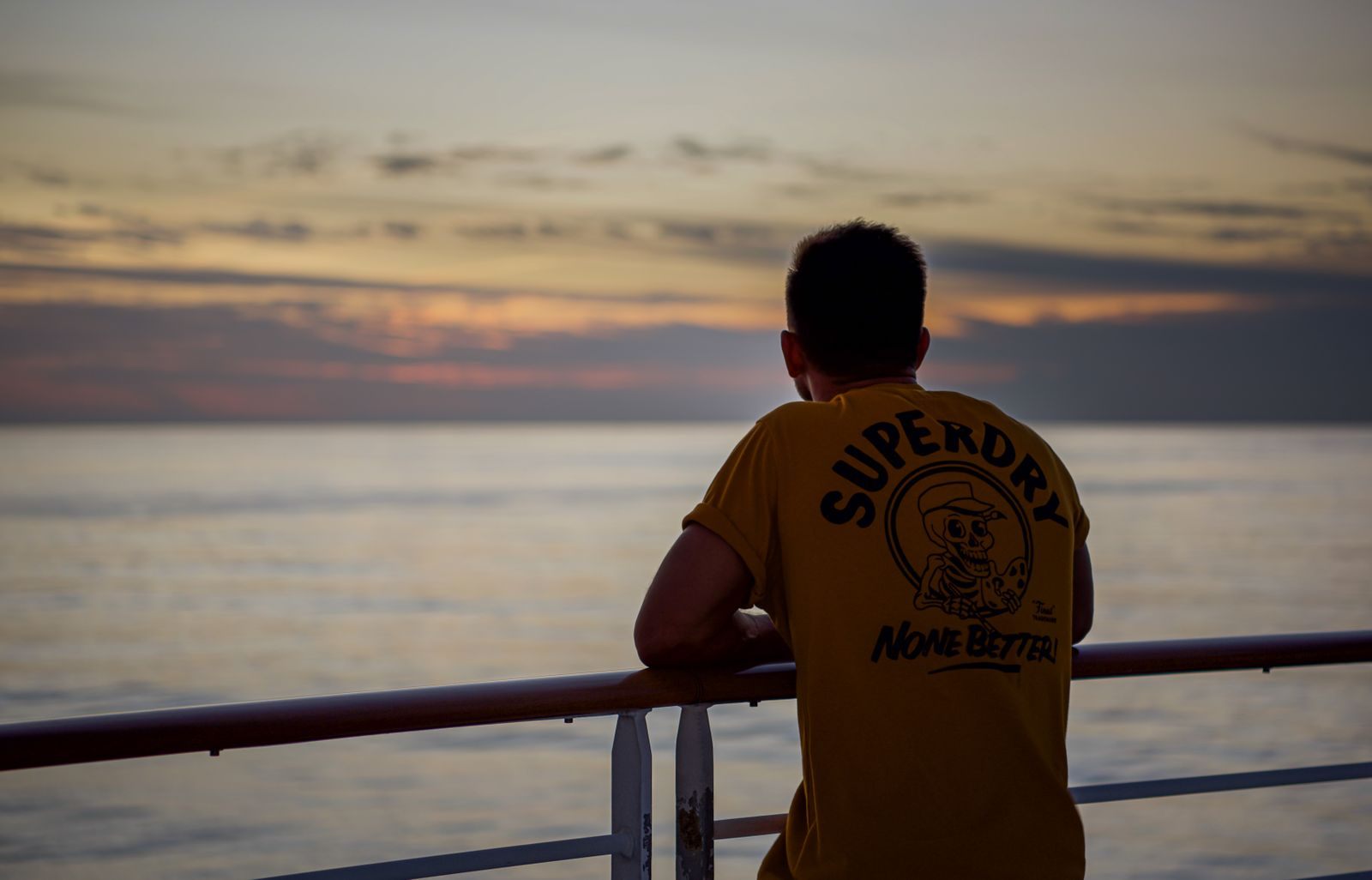 A cruiser at a ship’s rail watching the sea at sunset, the kind of moment a cruise survey asks you to rate